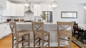 Une cuisine moderne avec des armoires blanches, un réfrigérateur en acier inoxydable et des tabourets de bar en bois.