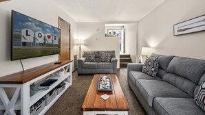 Uma sala de estar com televisão, dois sofás, uma mesa de centro e uma estante de livros.