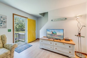 A room with a television, a wooden dresser, a yellow door, and a view of the outdoors.