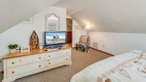 Ein Schlafzimmer mit Fernseher, Kommode, Sessel und Lampe.