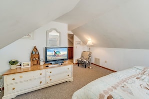 A bedroom with a TV, a dresser, a chair, and a lamp.