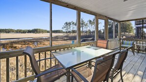 A covered outdoor area with a table and chairs, large windows offering views of a natural landscape.