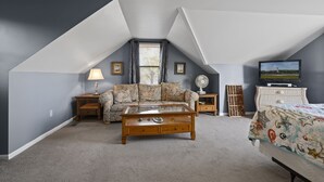 A cozy attic bedroom with a sloped ceiling, a floral sofa, a wooden coffee table, a TV, and a bed with a star-patterned duvet.