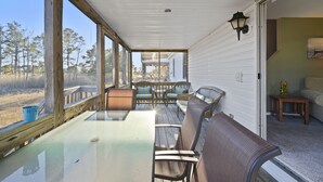 A covered porch with a glass table and wicker chairs, overlooking a natural landscape.