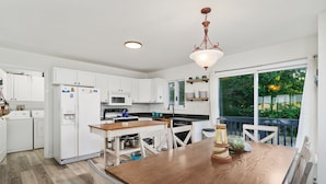 Une cuisine moderne avec des meubles blancs, une table à manger en bois et une vue sur la verdure à l’extérieur.