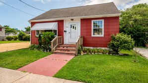 A single-story house with a red exterior, a front porch with a wooden railing, and a mailbox.