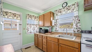 A kitchen with wooden cabinets, a sink, a stove, and a window with floral curtains.