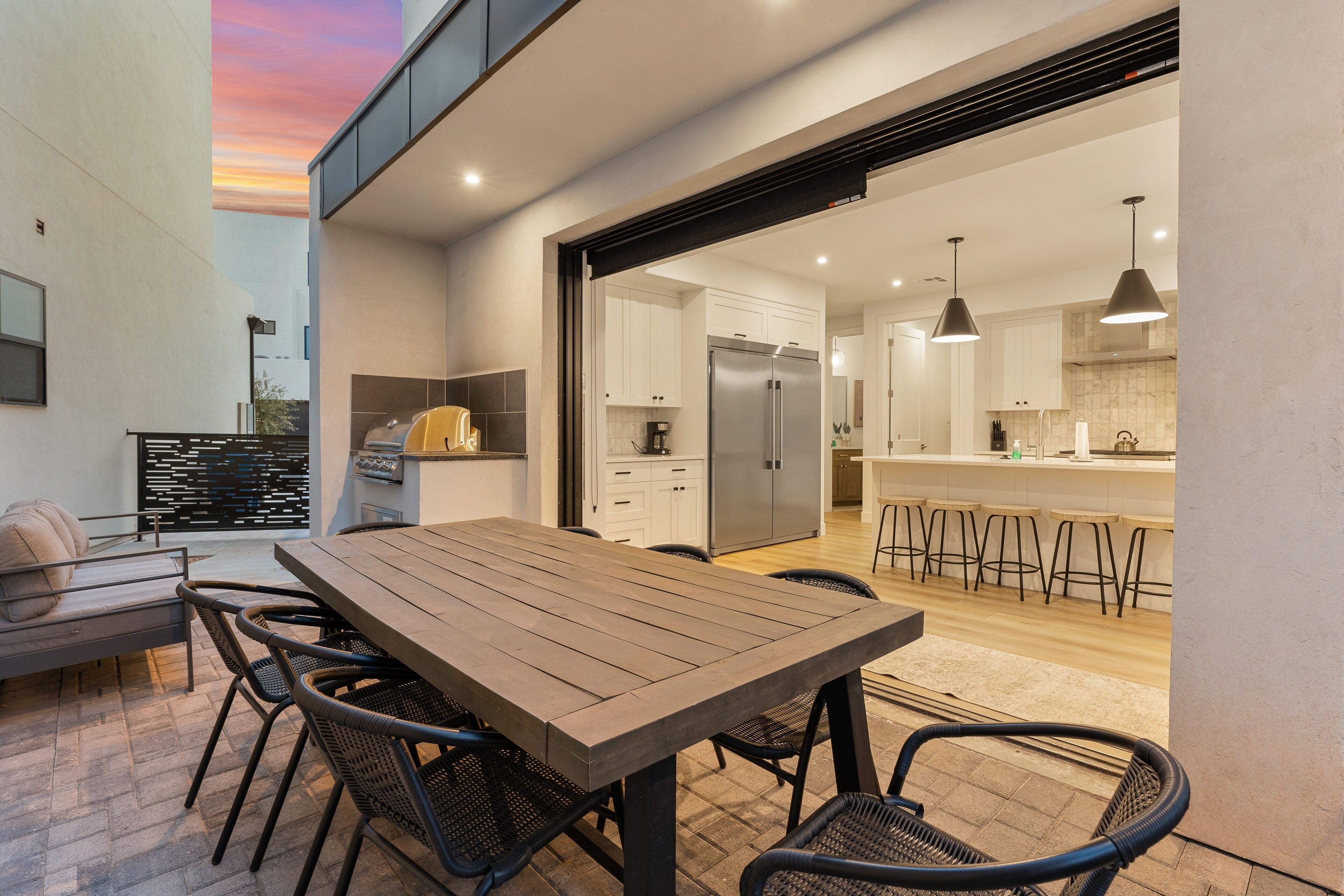A modern kitchen with white cabinets, a stainless steel refrigerator, and a bar area with stools.