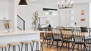 A modern kitchen with white cabinetry, a central island with stools, a chandelier, and a dining area with black chairs.