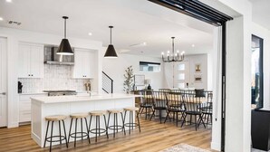 A modern kitchen with white cabinetry, a central island with stools, and a dining area with black chairs.