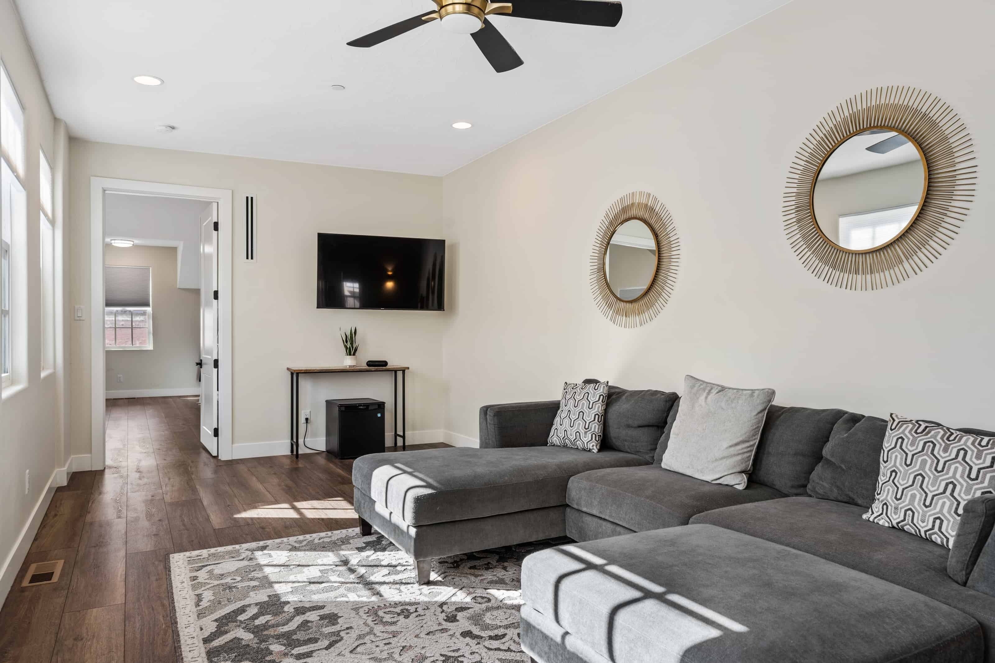 A modern living room with a grey sectional sofa, a fireplace, a flat-screen TV, and decorative mirrors on the walls.