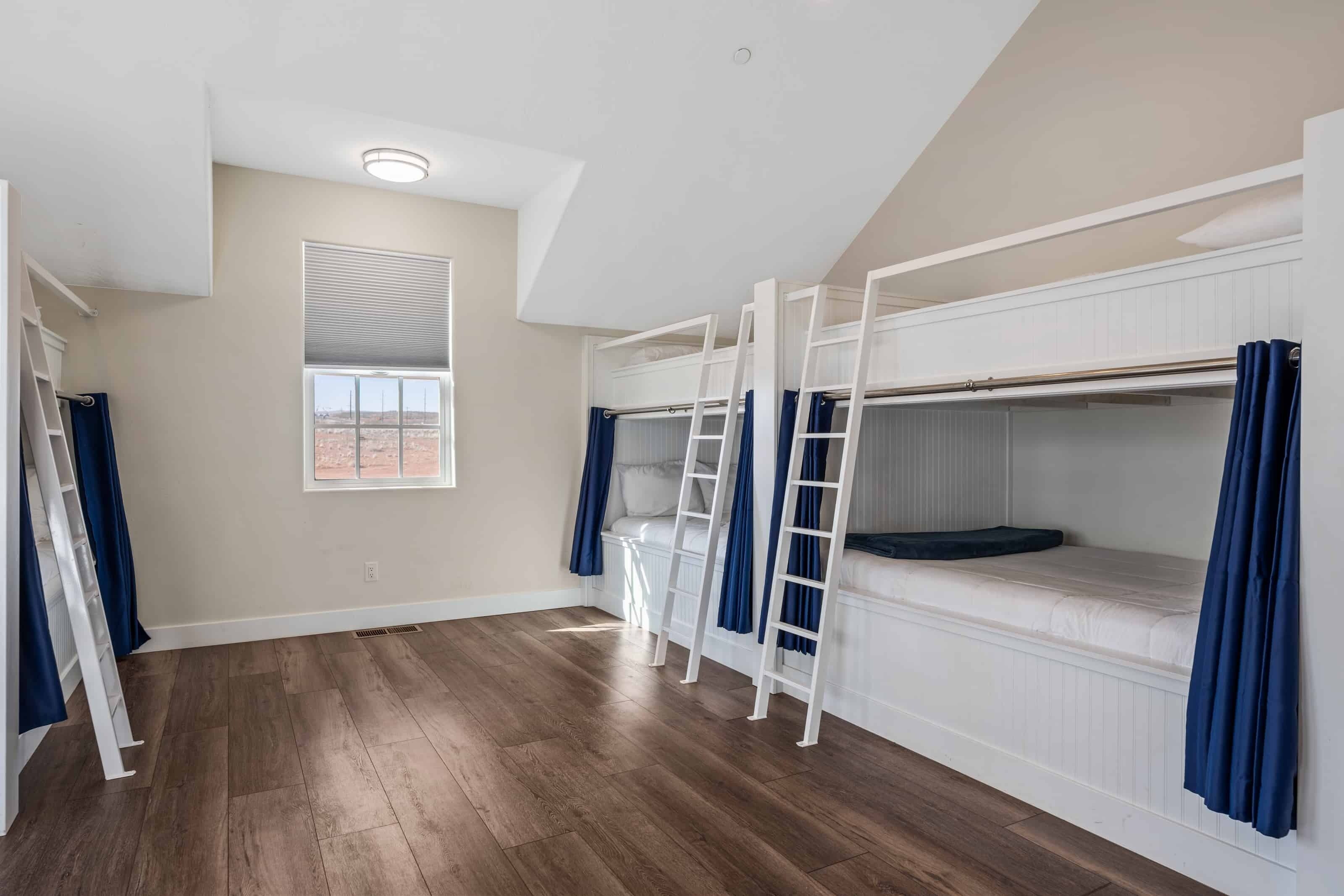 A room with bunk beds, a window with blinds, a ladder, and a white ceiling.
