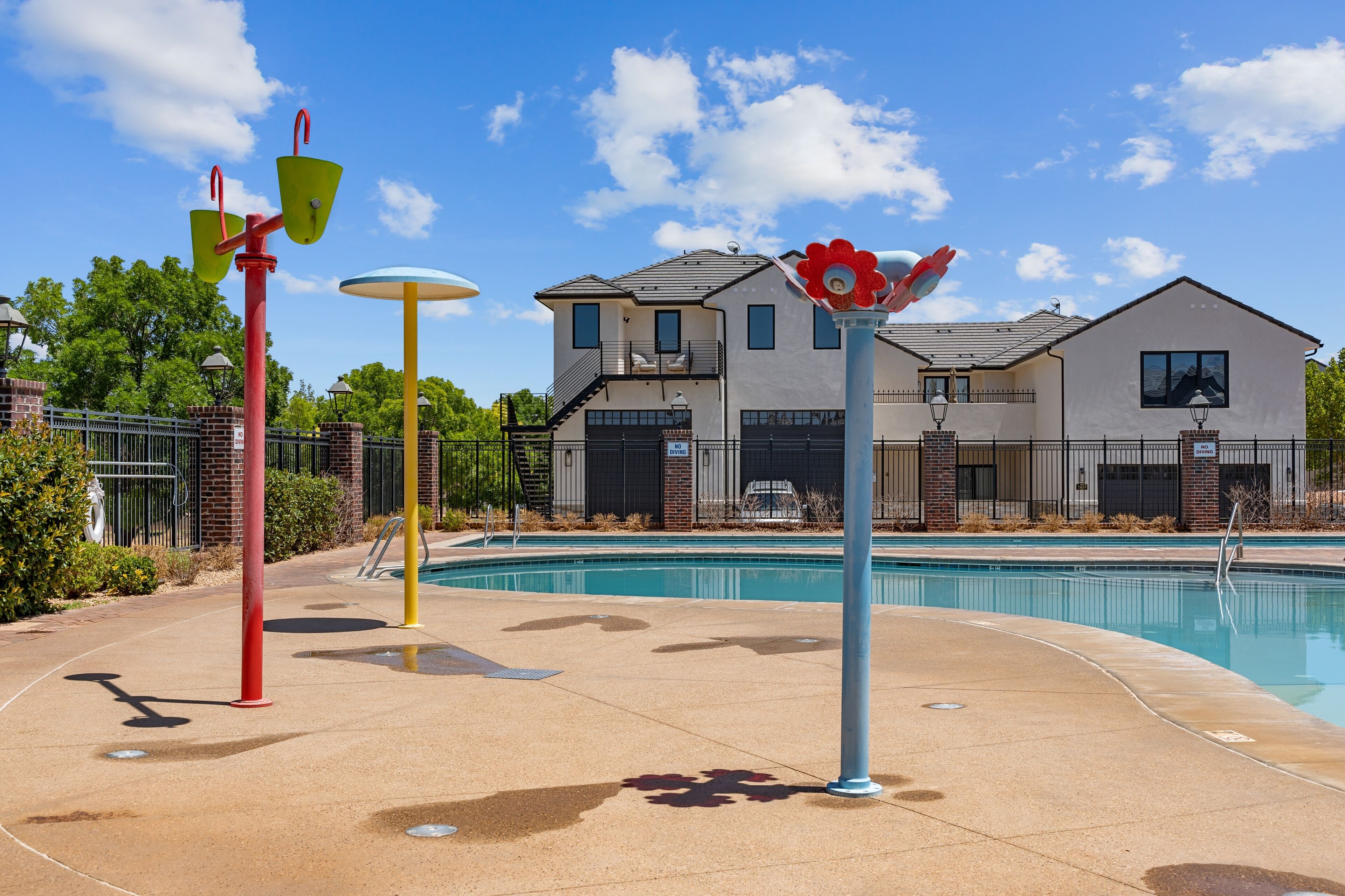 Area piscina con una casa sullo sfondo, attrezzature ginniche rosse e gialle e un palo decorativo blu e rosso.
