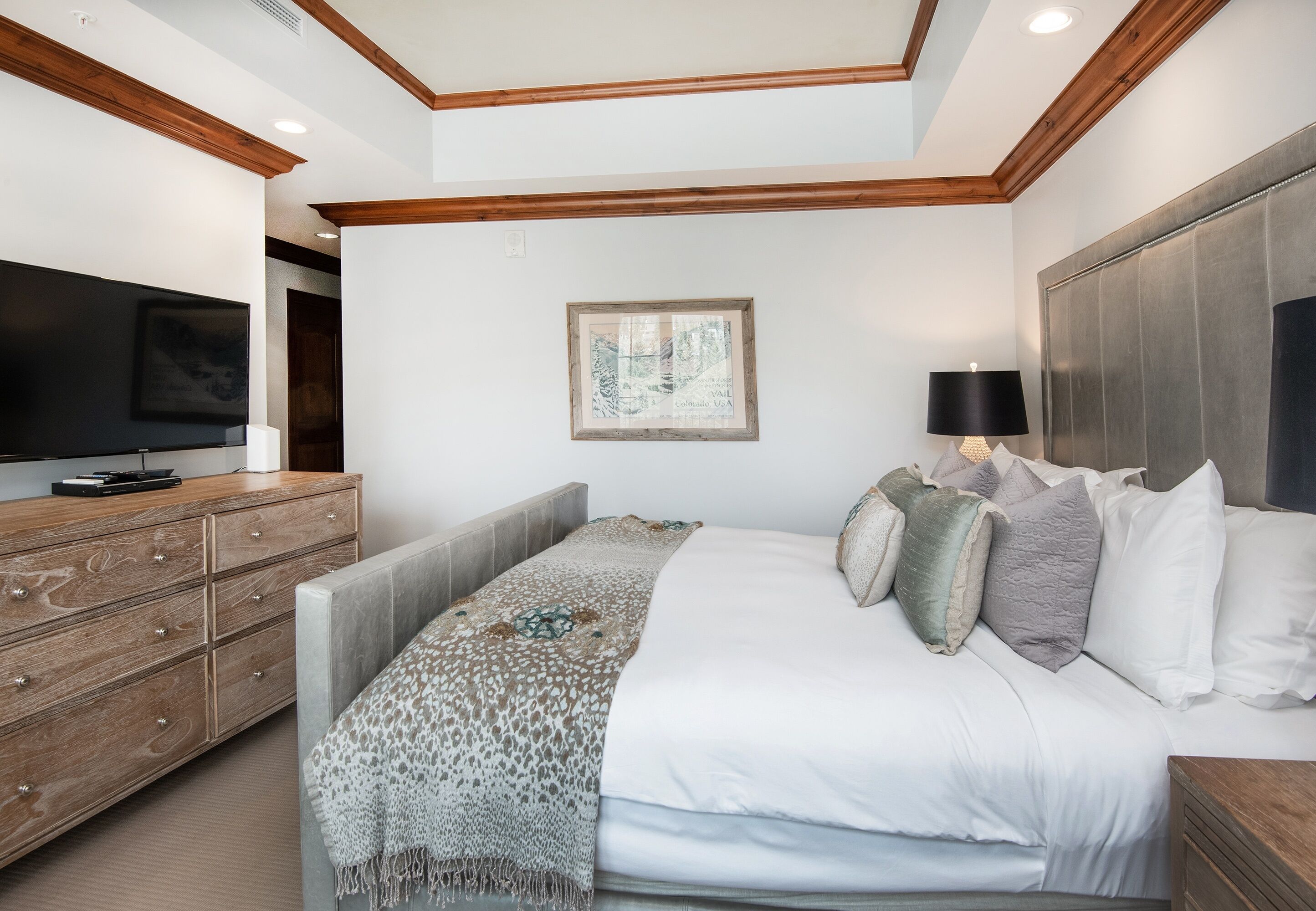 A modern bedroom with a large bed, wooden dresser, and a flat-screen TV.