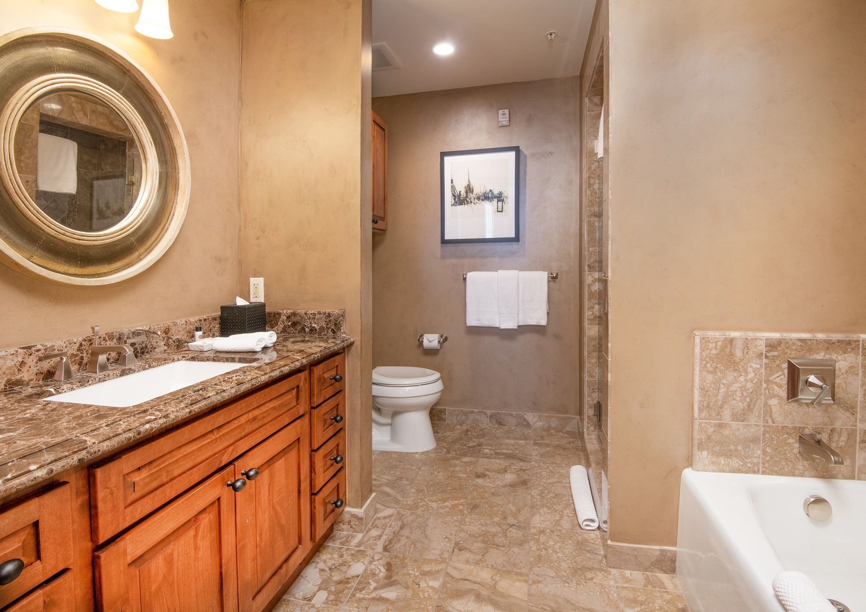 A bathroom with a marble sink, wooden vanity, a large mirror, a toilet, a shower area, and a bathtub.