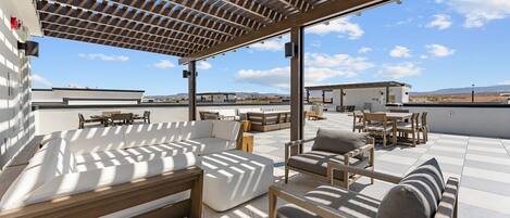 A rooftop terrace with outdoor seating, including sofas and chairs, under a pergola.