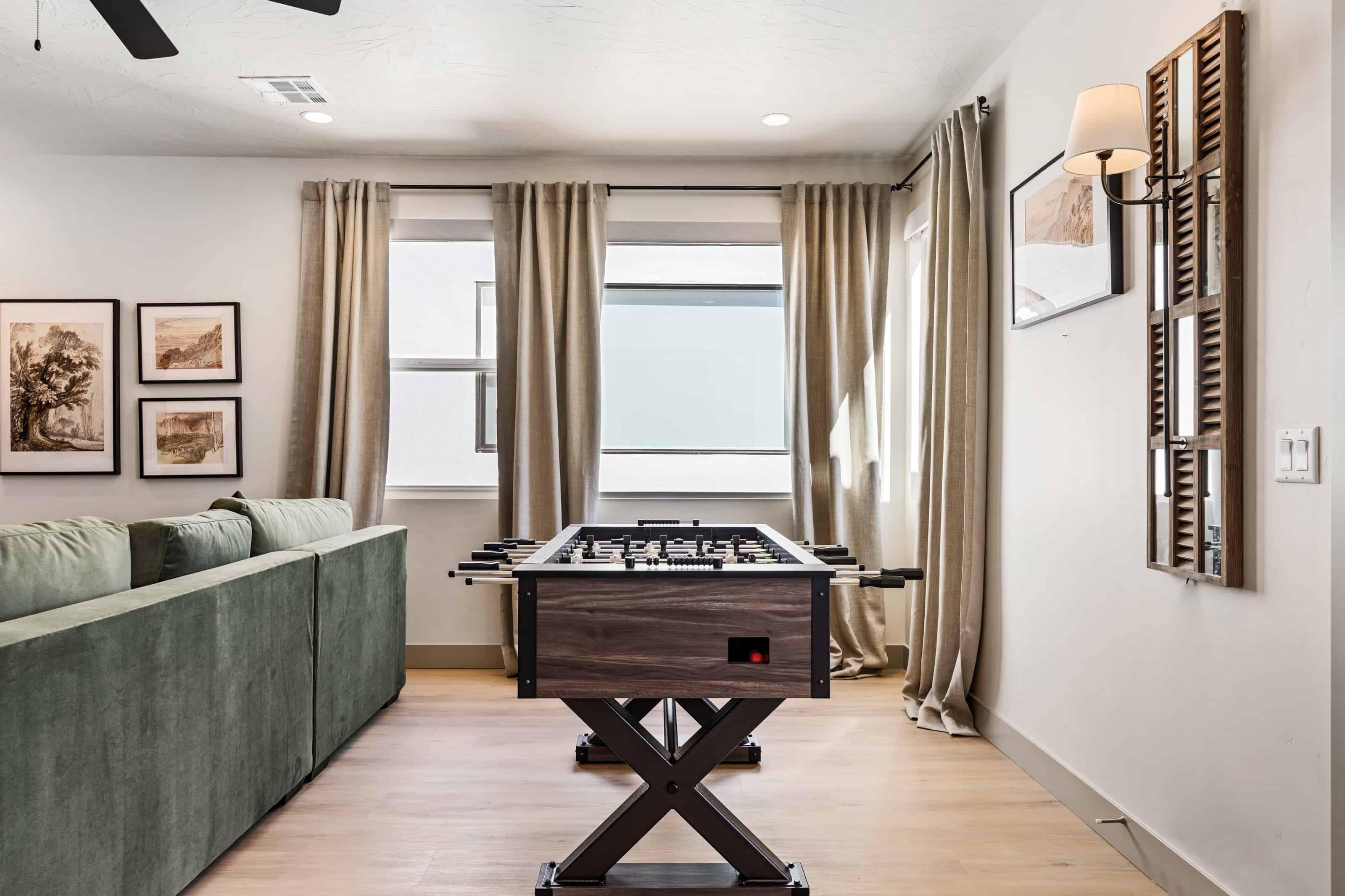 A room with a foosball table, a sofa, and a window with curtains.