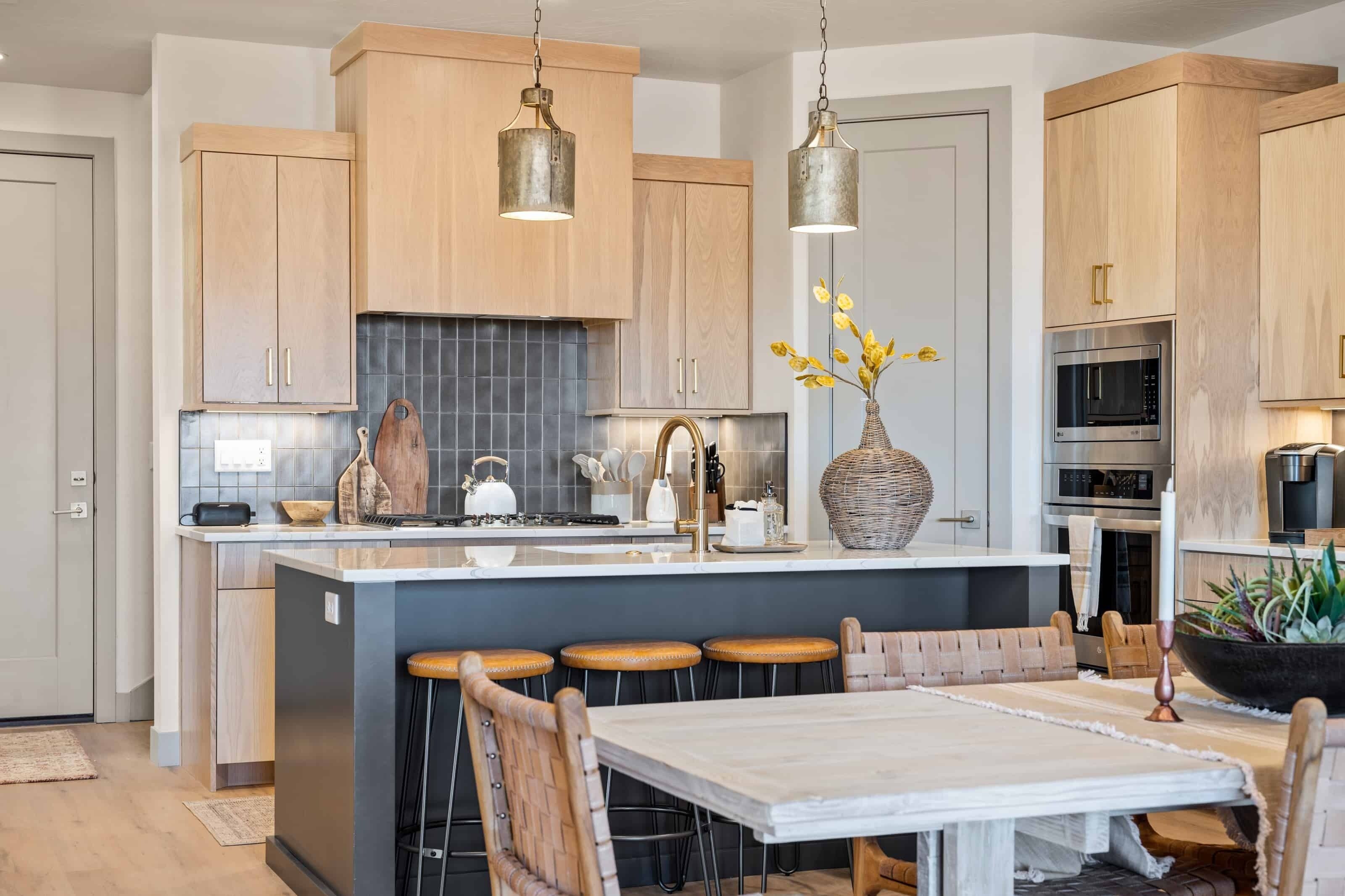 A modern kitchen with wooden cabinets, a central island with stools, stainless steel appliances, and pendant lighting.