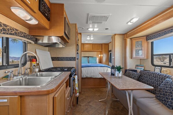 Un intérieur de camping-car compact comprenant un coin cuisine, un lit et un espace salon.