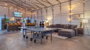 A spacious indoor area with a ping pong table, seating, and a television displaying a sports event. - The Ranger Station + Club House w/Hot Tub (Joshua Tree)