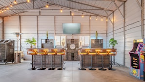 A bar area with four stools, a television mounted on the wall, and arcade games. - The Ranger Station + Club House w/Hot Tub (Joshua Tree)
