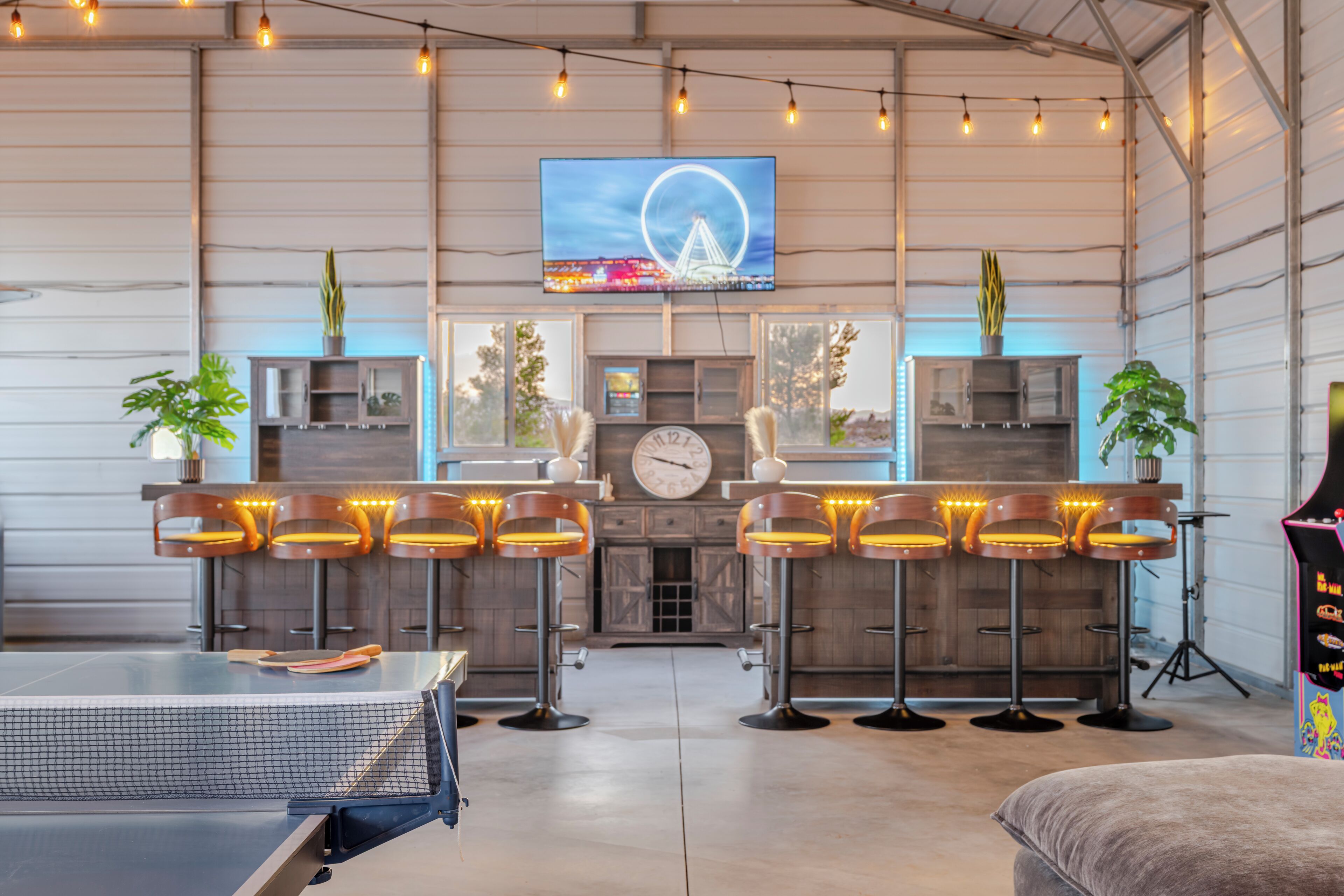 A spacious bar area with high stools, a large TV screen, and a clock on the wall.