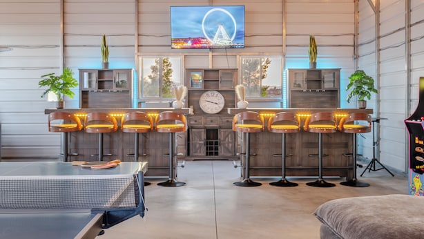 A spacious bar area with high stools, a large TV screen, and a clock on the wall. - The Ranger Station + Club House w/Hot Tub (Joshua Tree)