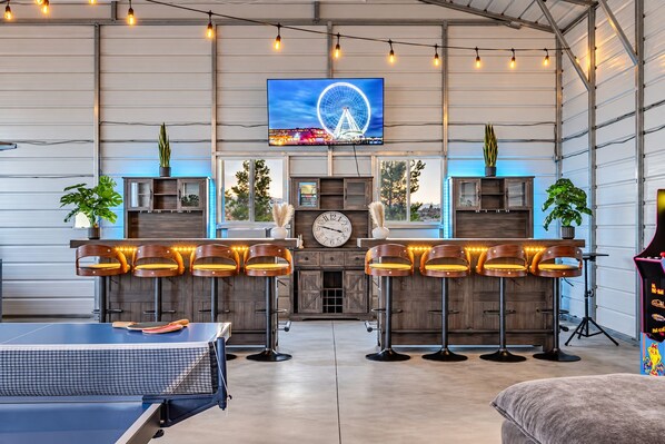 A spacious room with a ping pong table, bar stools, and a large TV screen displaying a Ferris wheel.