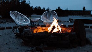 A fire pit with three white chairs around it, set in a sandy area with trees in the background. - The Ranger Station + Club House w/Hot Tub (Joshua Tree)