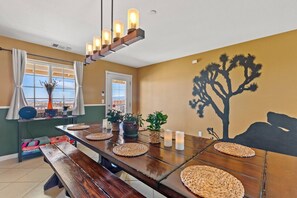 A dining area with a long wooden table, woven placemats, candles, and a wall mural of a tree.