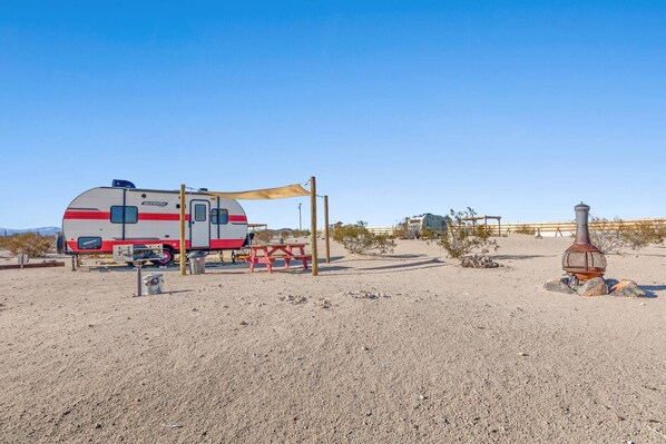 A caravan parked in a desert setting with a picnic table and a barbecue grill. - JT Village Campground - Sun Ray (Joshua Tree)