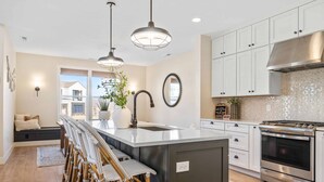 A modern kitchen with a central island, stainless steel appliances, and a seating area with wicker chairs. - Forever No Bad Days 6 Bedroom Townhouse (St. George)