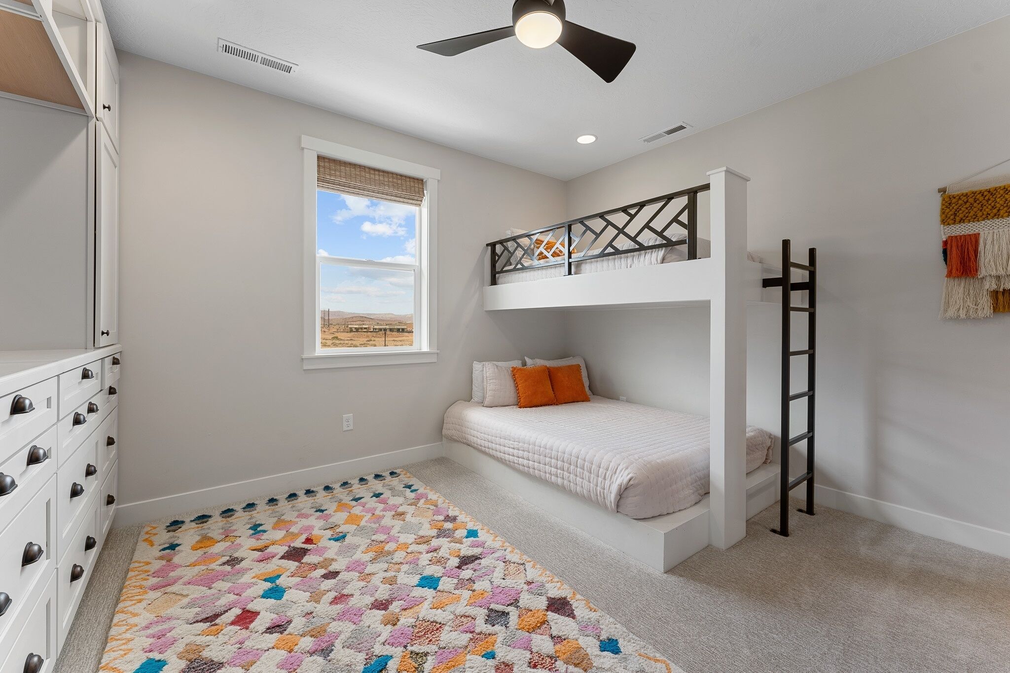 A bedroom with a bunk bed, a ladder, a window with a view, and a patterned rug.