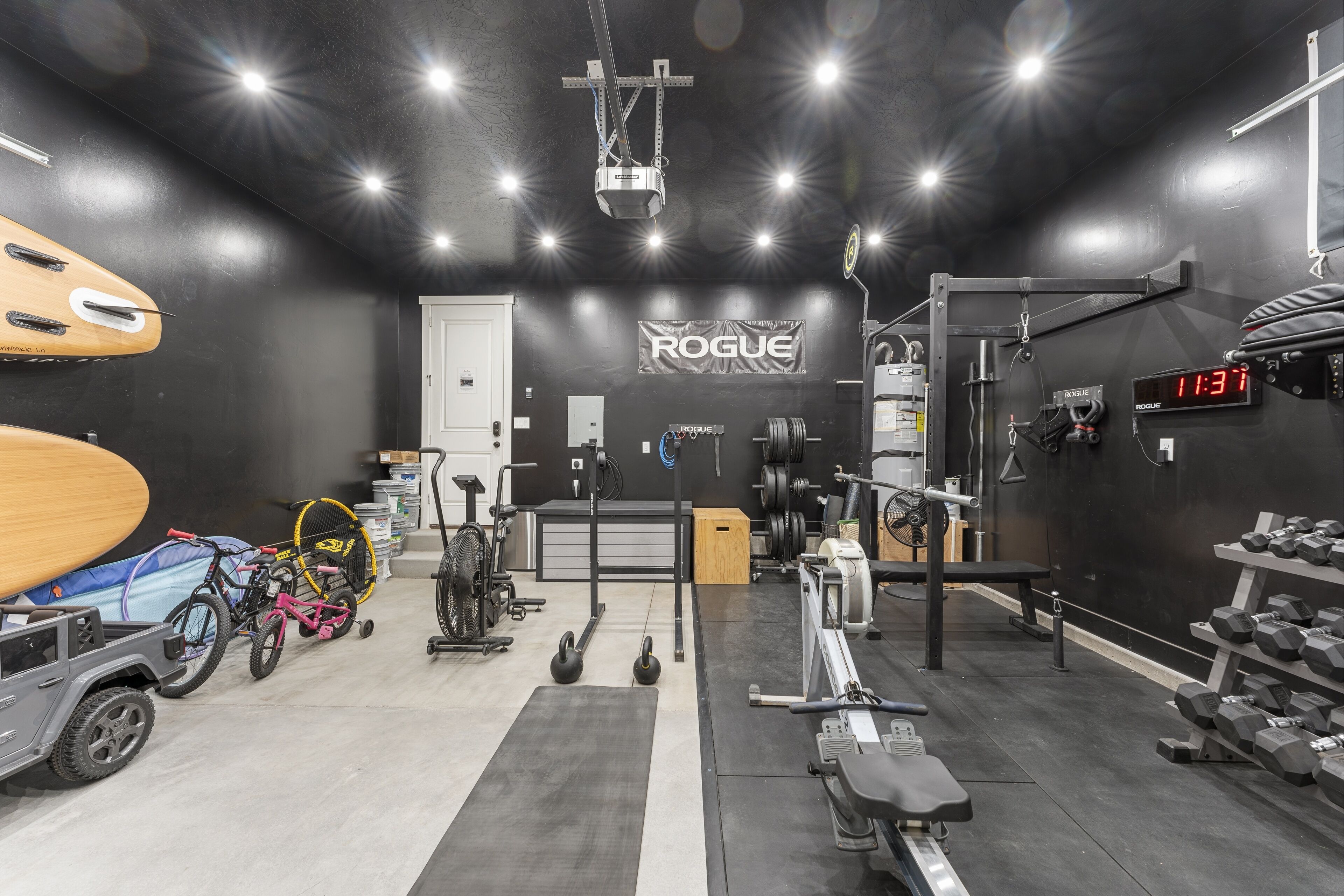 A gym with a black and white color scheme, weightlifting equipment, a wall-mounted digital clock, and a ceiling-mounted projector.