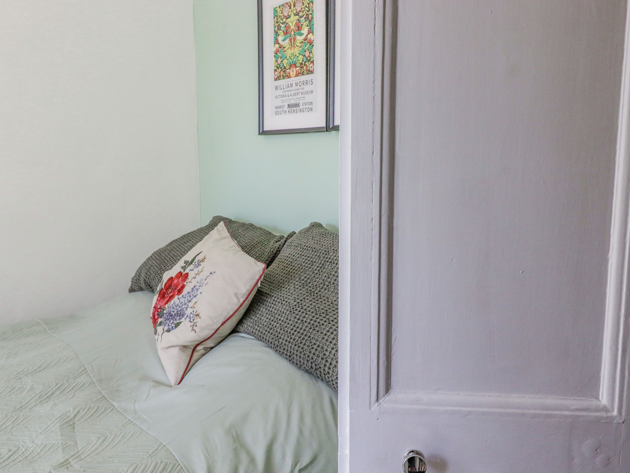 Un dormitorio con una cama, almohadas, un cuadro en la pared y una puerta.