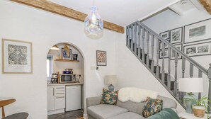 A cozy living room with a grey sofa, a wooden chair, and a staircase leading to a kitchen area. - 4 Pulmans Place (Halifax)