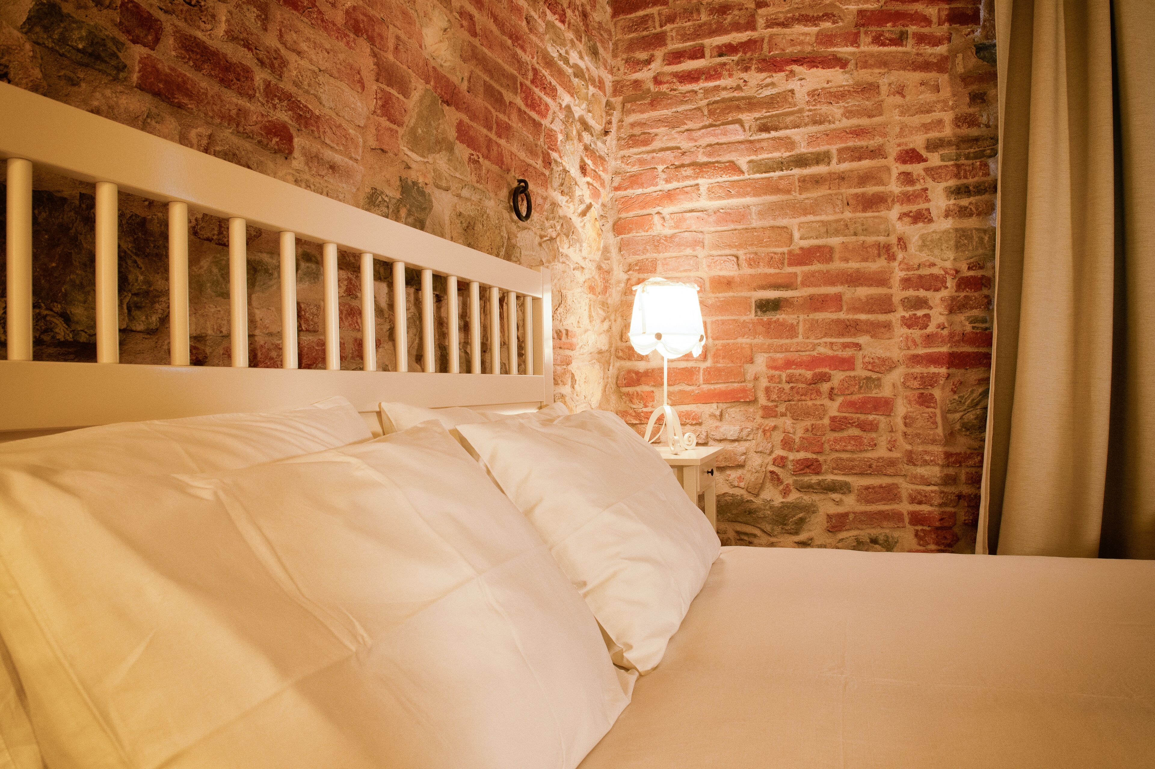 A bed with white bedding in a room with a brick wall and a white headboard.
