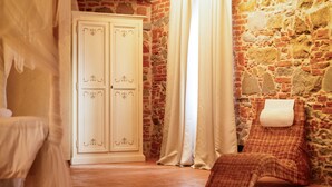 Une pièce avec un mur en pierre, une armoire blanche et un fauteuil en osier.