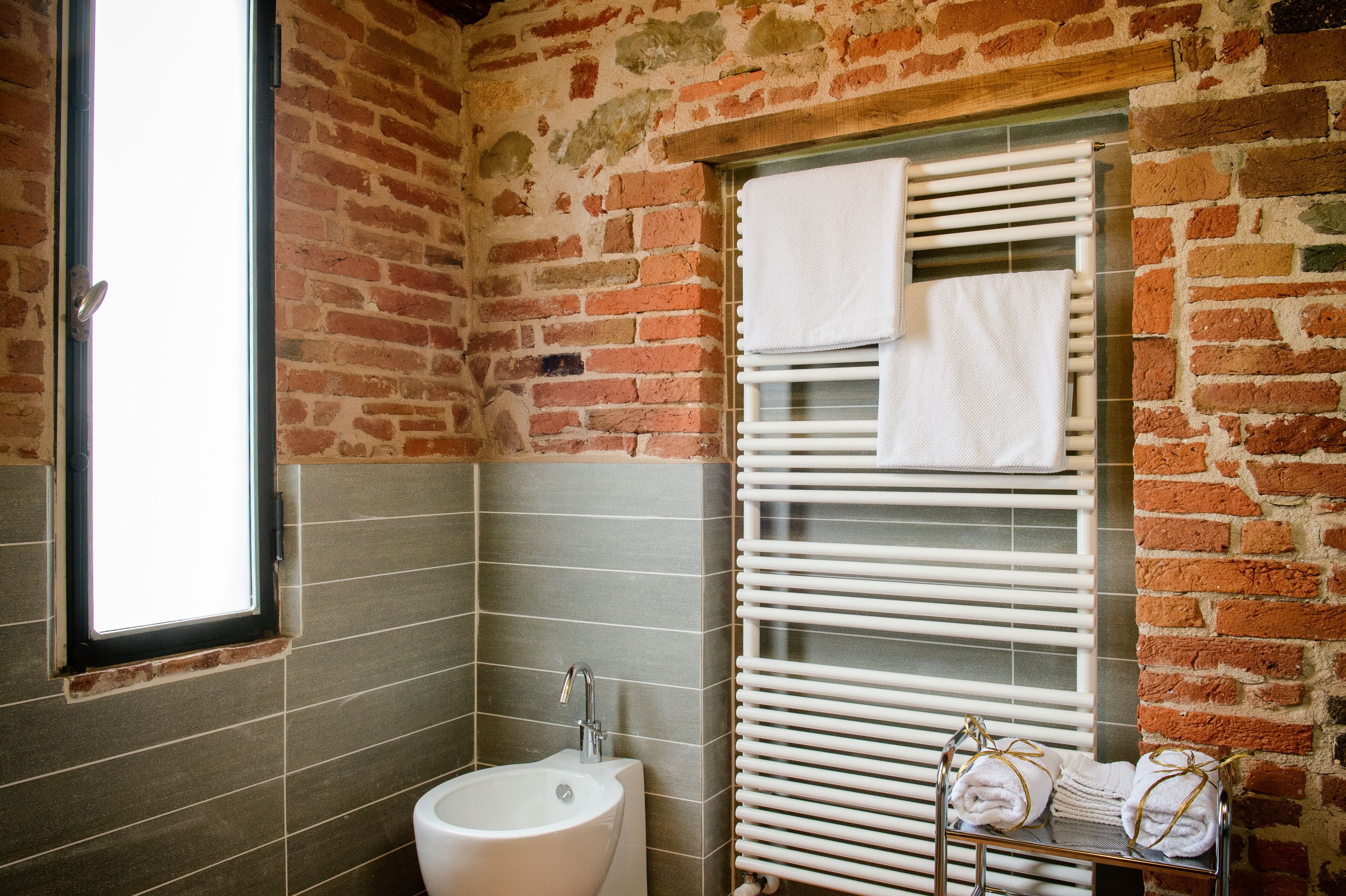 A bathroom with a brick wall, a window, a sink, and a towel rack with towels.