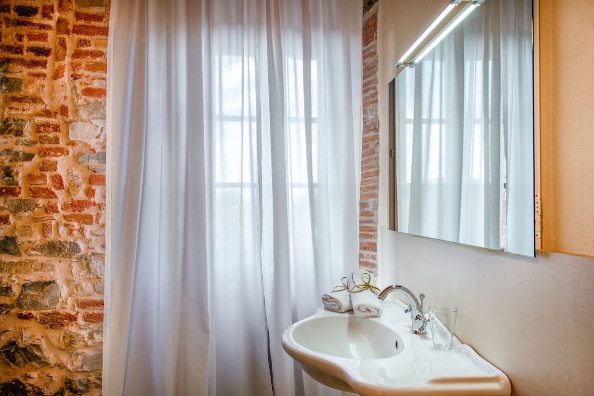 Ein Badezimmer mit einem weißen Waschbecken, einem Spiegel und einem Fenster mit weißen Vorhängen.