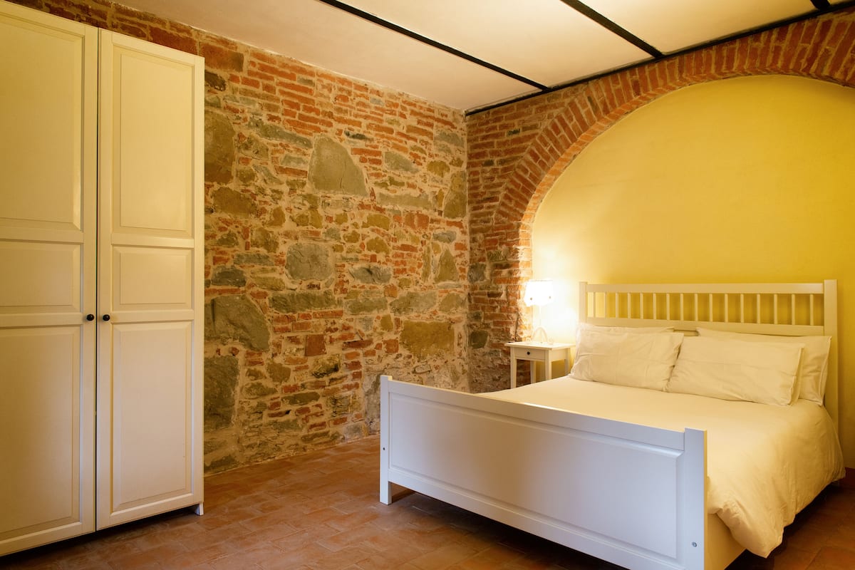 Ein Schlafzimmer mit Steinwand, einem weißen Bett und einem Kleiderschrank.
