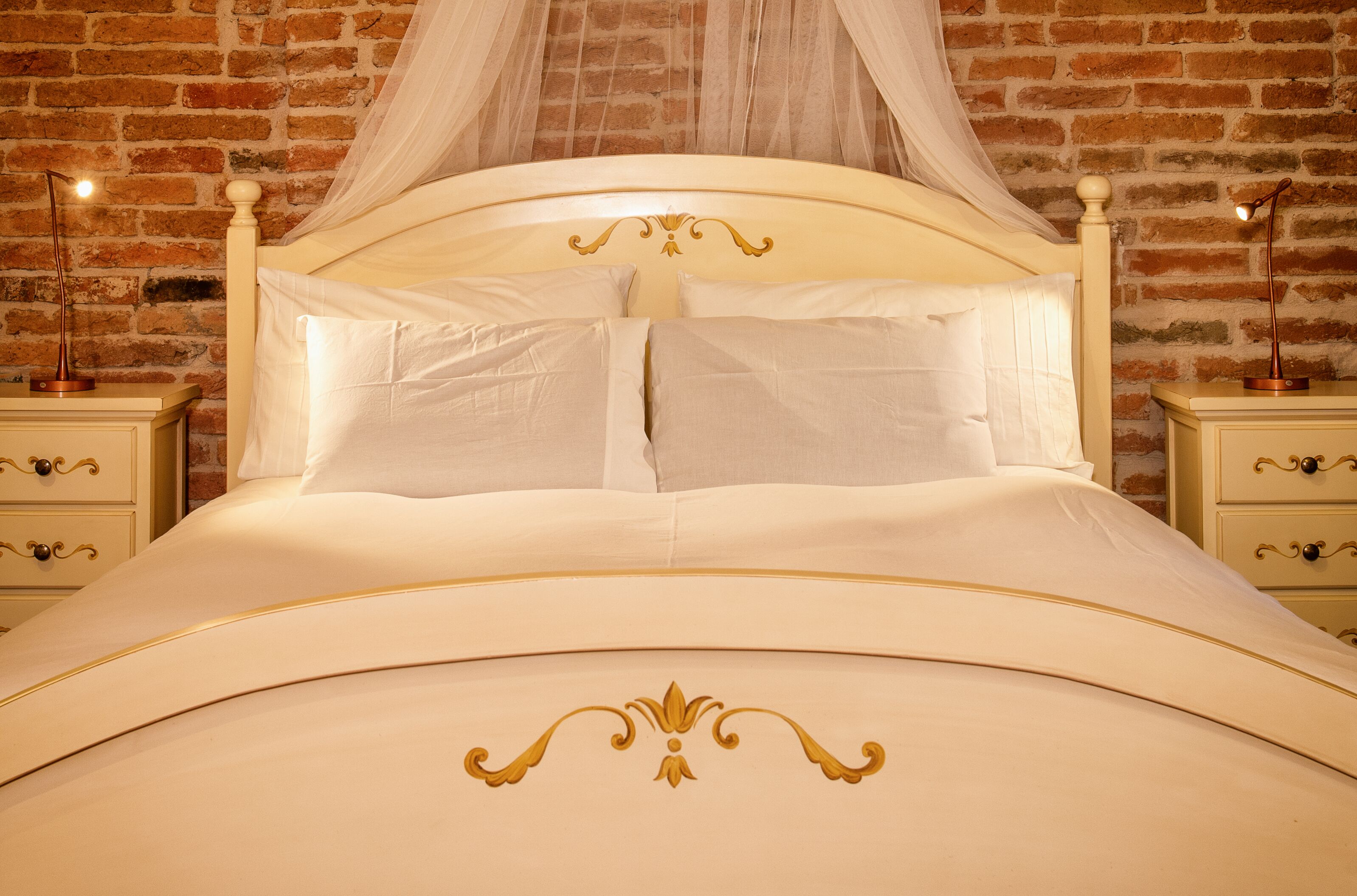 A bed with a canopy, two bedside tables, and a brick wall background.