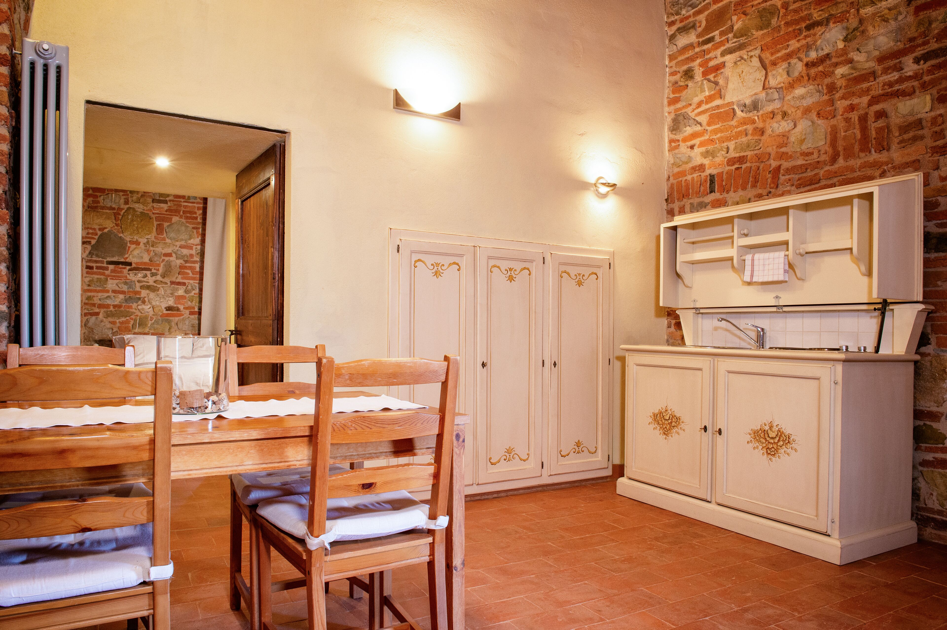 A room with a wooden dining table and chairs, a white cabinet with drawers, and a brick wall.