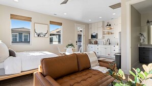 Un dormitorio con cama, un sofá de cuero marrón, ventilador de techo y vistas al exterior.