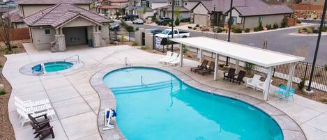 A residential area with a large swimming pool, lounge chairs, and a covered patio area.