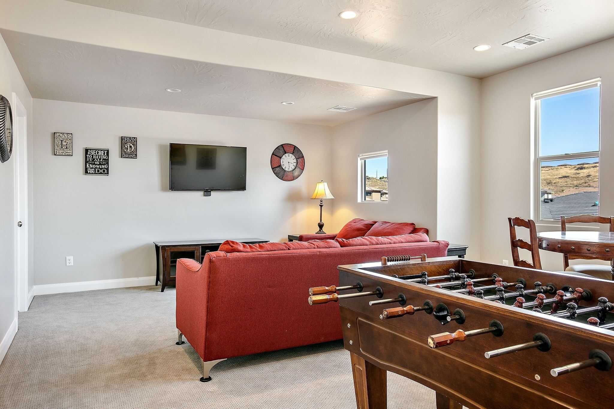A living room with a red sofa, a foosball table, a TV, and a window with a view.