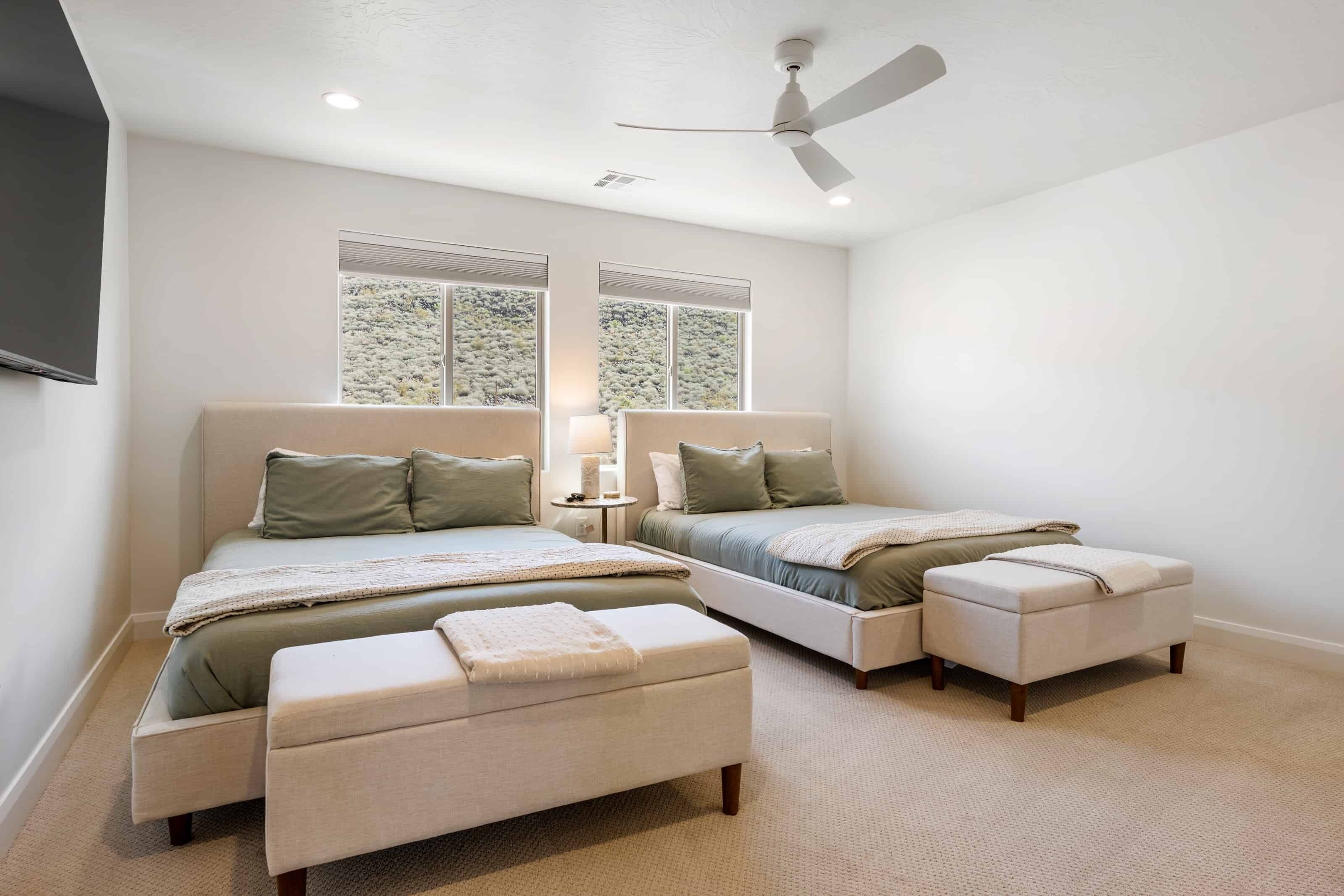 A bedroom with two beds, a ceiling fan, and large windows.