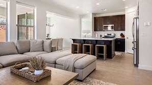 A modern living room with a sectional sofa, a coffee table with decorative items, and a view to the kitchen area. - Hygge House 5 Bedroom Home (Washington)