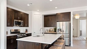 A modern kitchen with dark wood cabinets, stainless steel appliances, and a large island with a sink. - Hygge House 5 Bedroom Home (Washington)
