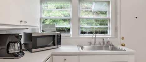 A kitchen with white cabinets, a microwave, a coffee maker, and a sink.